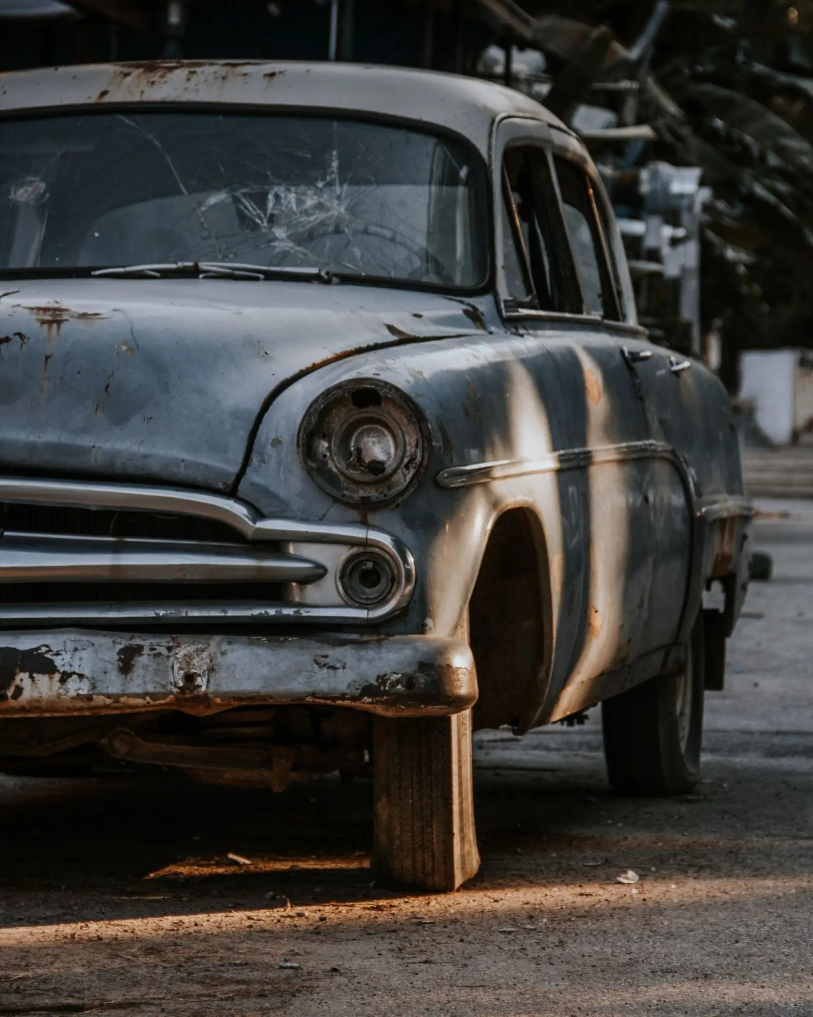 A rusted old sedan with a cracked windshield, propped on a wooden block at the curb
