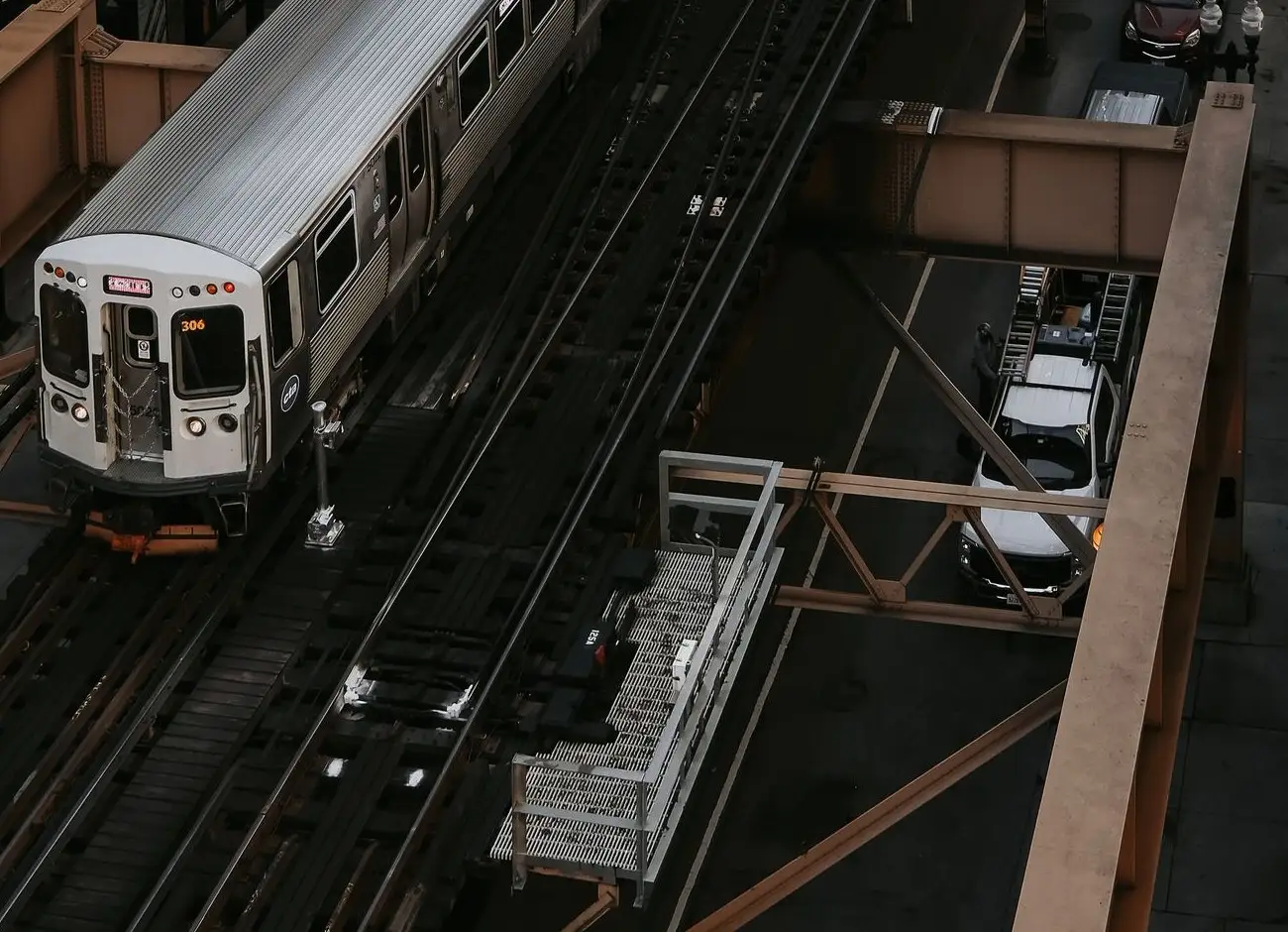 A CTA train on elevated tracks above a Chicago street, with parked cars below
